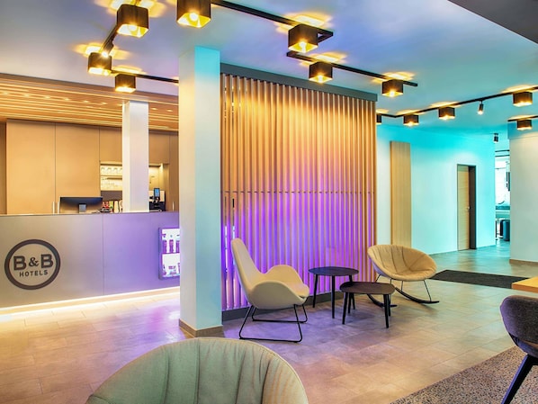 Un moderno vestíbulo de hotel con mostrador de recepción, zona de estar y una pared decorativa con persianas verticales.