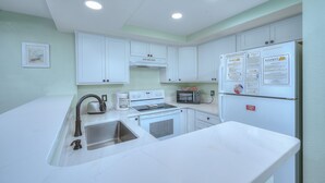 Une cuisine avec des meubles blancs, un évier en acier inoxydable, un four à micro-ondes, un four et un réfrigérateur.