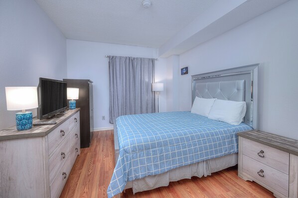 A bedroom with a bed, a TV on a dresser, and a nightstand.