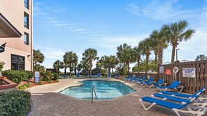 A pool area with lounge chairs, palm trees, and a building with a sign indicating no lifeguard on duty.