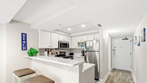 A modern kitchen with white cabinetry, a central island with stools, a microwave, and a refrigerator.