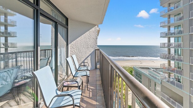 A balcony with chairs and a table overlooking a beach.