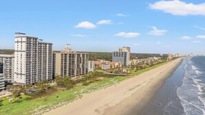 A coastal cityscape with high-rise buildings, a sandy beach, and a clear sky.