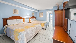 Ein Hotelzimmer mit zwei Betten, einem Holzkleiderschrank, einem Fernseher und gerahmten Bildern an der Wand.