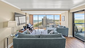 Ein modernes Wohnzimmer mit einem Klavier, einer Couch, einem Couchtisch und Meerblick durch große Fenster.