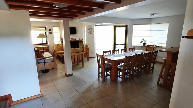 Amplia sala de estar con techo de madera, una mesa de comedor rodeada de sillas y un sofá al fondo.