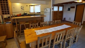 Un comedor con mesa y sillas de madera, una cocina al fondo y una lámpara en el techo.