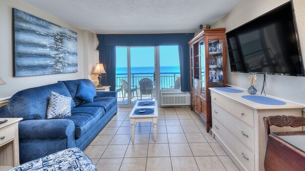 A living room with a blue sofa, a coffee table, a TV, and a view of the ocean. - Boardwalk Beach Resort #932 Gorgeous1 Bedroom Oceanfront Condo (Myrtle Beach)