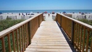 Une promenade en bois menant à une plage où se trouvent des gens et des parasols.