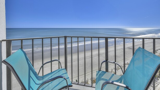 Un balcon avec deux chaises bleues donnant sur une plage.