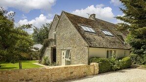 A stone house with a sloped roof, a gravel driveway, and a well-maintained lawn. - Cats Abbey Cottage a charming,  Northleach , Gloucestershire (Northleach)