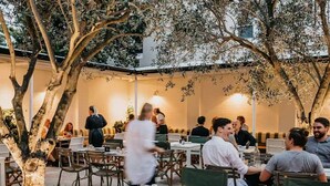 An outdoor dining area with tables and chairs, surrounded by trees and a building in the background. - ★ Sunshine Loft With Balcony by ★ Sydney Dreams ★ (Bondi Beach)
