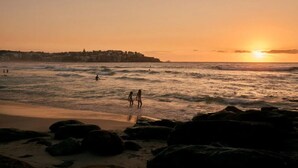 A beach scene with waves, a sunset, and a distant shoreline. - ★ Sunshine Loft With Balcony by ★ Sydney Dreams ★ (Bondi Beach)