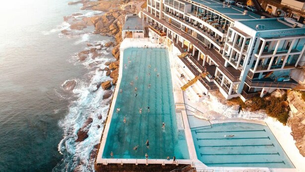 A large outdoor swimming pool adjacent to a building with multiple balconies, overlooking the ocean. - ★ Sunshine Loft With Balcony by ★ Sydney Dreams ★ (Bondi Beach)