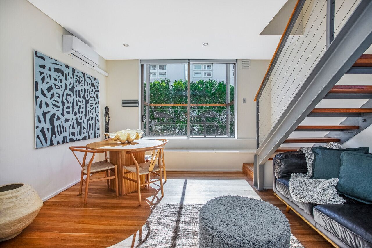 A modern living room with a wooden dining table, a sofa, and a staircase.