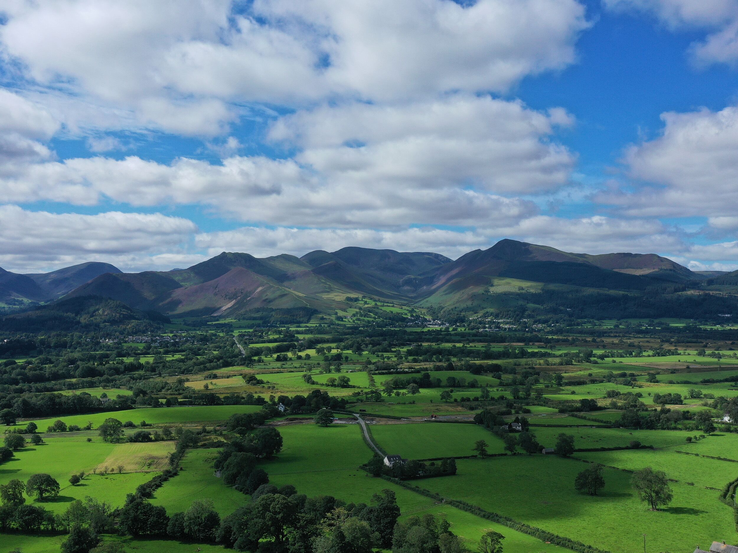 A panoramic view of a valley with rolling hills, a small village, and a road leading through the landscape.