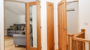A hallway with wooden doors leading to a living area with a sofa and a coat rack. - Norton (Keswick)