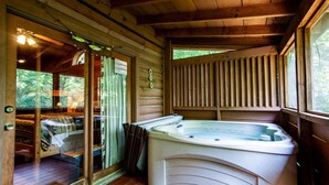 A wooden cabin interior with a hot tub, a glass door leading to an outdoor area, and a wooden ceiling.
