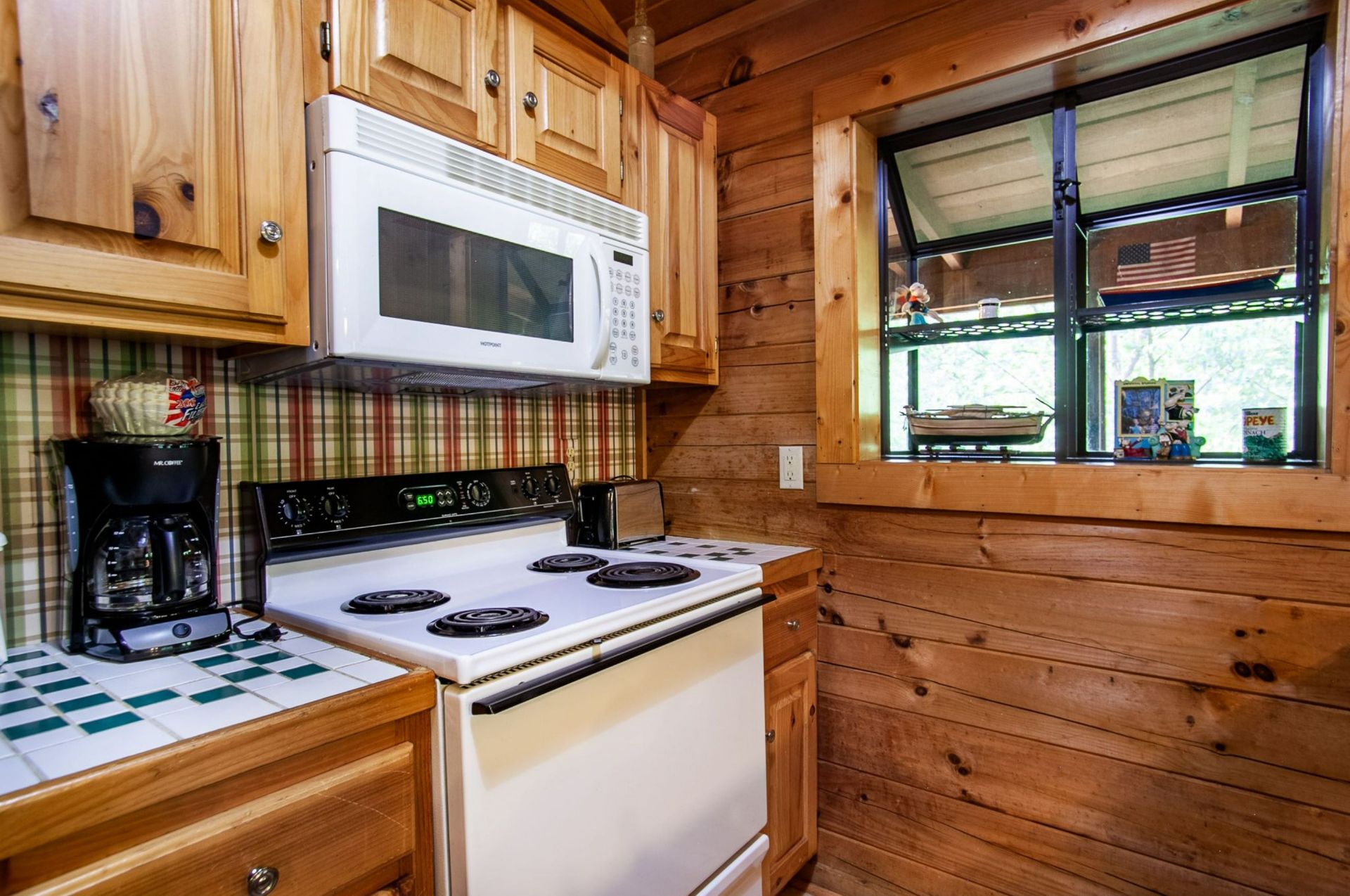 A kitchen with wooden cabinets, a white stove, a microwave, and a window with a view of the outdoors.