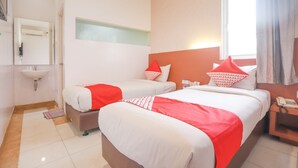 A hotel room with two beds, a bedside table with a phone, a small desk with a lamp, a window with curtains, and a bathroom with a sink and mirror. - OYO 172 Gunung Sahari 12 Residence (Jakarta)