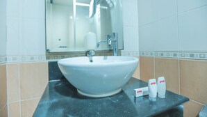 A bathroom with a large white sink, a mirror, and a towel dispenser. - OYO 172 Gunung Sahari 12 Residence (Jakarta)