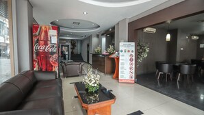 A hotel lobby with a reception desk, a Coca-Cola advertisement, a reception area with a flower arrangement, and a seating area with a sofa and a coffee table. - OYO 172 Gunung Sahari 12 Residence (Jakarta)