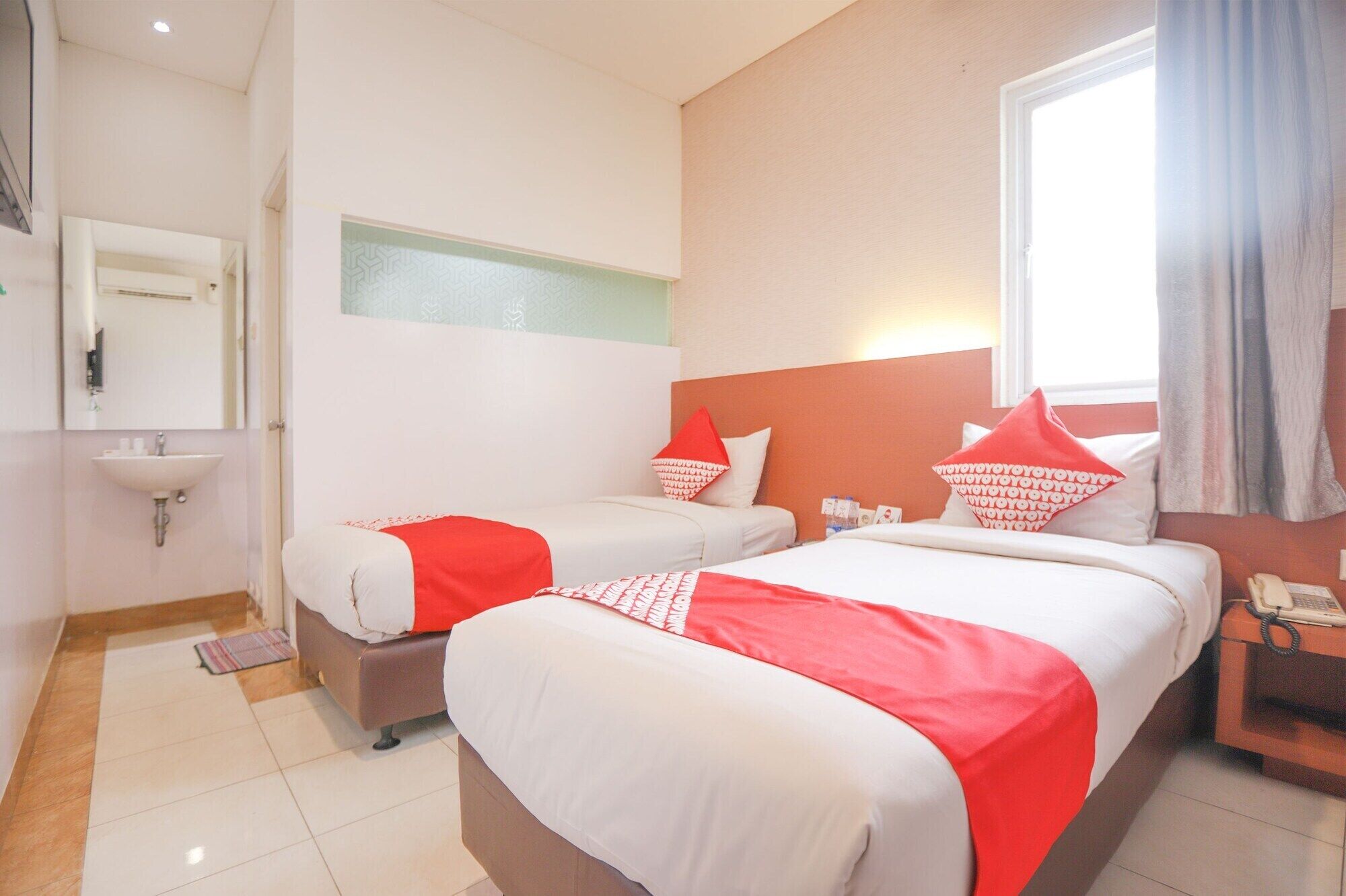 A hotel room with two beds, a sink, and a window with curtains.