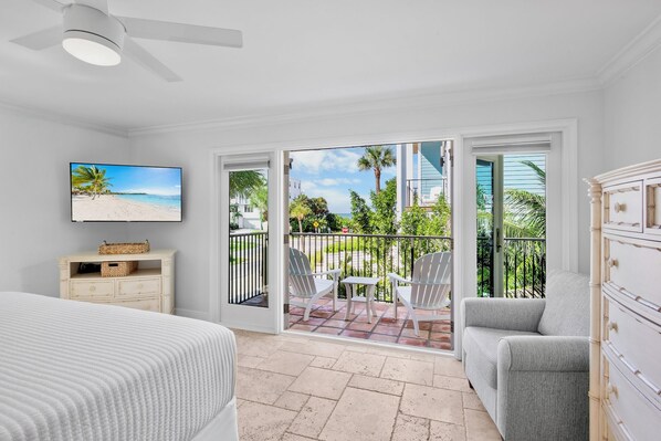 A bedroom with a bed, a TV, a dresser, and a balcony with a view of the beach.