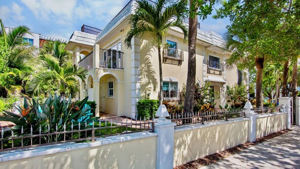 A two-story building with a balcony, surrounded by palm trees and a white fence. - Luxury Pool and Rooftop Deck, Walk to Siesta Key Beach and Village! - Casa Siest (Siesta Key)