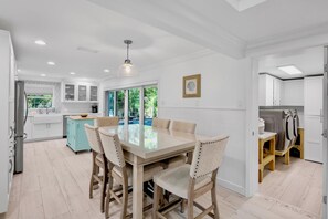 A modern kitchen with white cabinets, a dining area with a glass table, and a view of a pool. - Luxury Pool and Rooftop Deck, Walk to Siesta Key Beach and Village! - Casa Siest (Siesta Key)