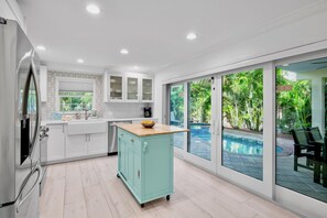 A modern kitchen with a built-in refrigerator, a wooden countertop, and a view of a swimming pool through large sliding glass doors.