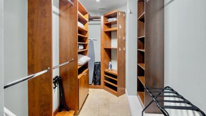 A walk-in closet with multiple wooden shelves and hanging space, a folding chair, and a visible ironing board. - Luxury Pool and Rooftop Deck, Walk to Siesta Key Beach and Village! - Casa Siest (Siesta Key)