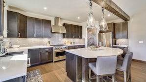 A modern kitchen with dark cabinets, stainless steel appliances, a central island with seating, and pendant lighting. - Cocoa Cabin: New Baldy Mtn Home, Hot Tub & Steam Shower, EV Charger! (Breckenridge)