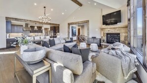 A spacious living room with a modern fireplace, a large flat-screen TV mounted above it, and a cozy seating area with a large sectional sofa and ottomans. - Cocoa Cabin: New Baldy Mtn Home, Hot Tub & Steam Shower, EV Charger! (Breckenridge)