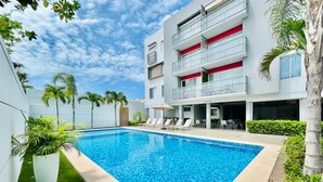 Une piscine avec des chaises longues, un bâtiment doté de balcons et des palmiers.