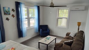 Ett vardagsrum med en brun soffa, en blå fåtölj, ett soffbord och ett matbord med bordsunderlägg.