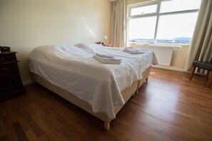 A double bed with a white bedspread, two folded towels, a wooden dresser, and a view of the outdoors through a window. - Sel-hotel Myvatn (Myvatn)