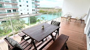 Un balcón con mesa y bancos de madera, con vistas a un cuerpo de agua y edificios.