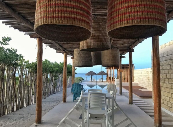 Relax in a tranquil beachside setting with a clear ocean view, surrounded by comfortable seating and a scenic path to the beach.