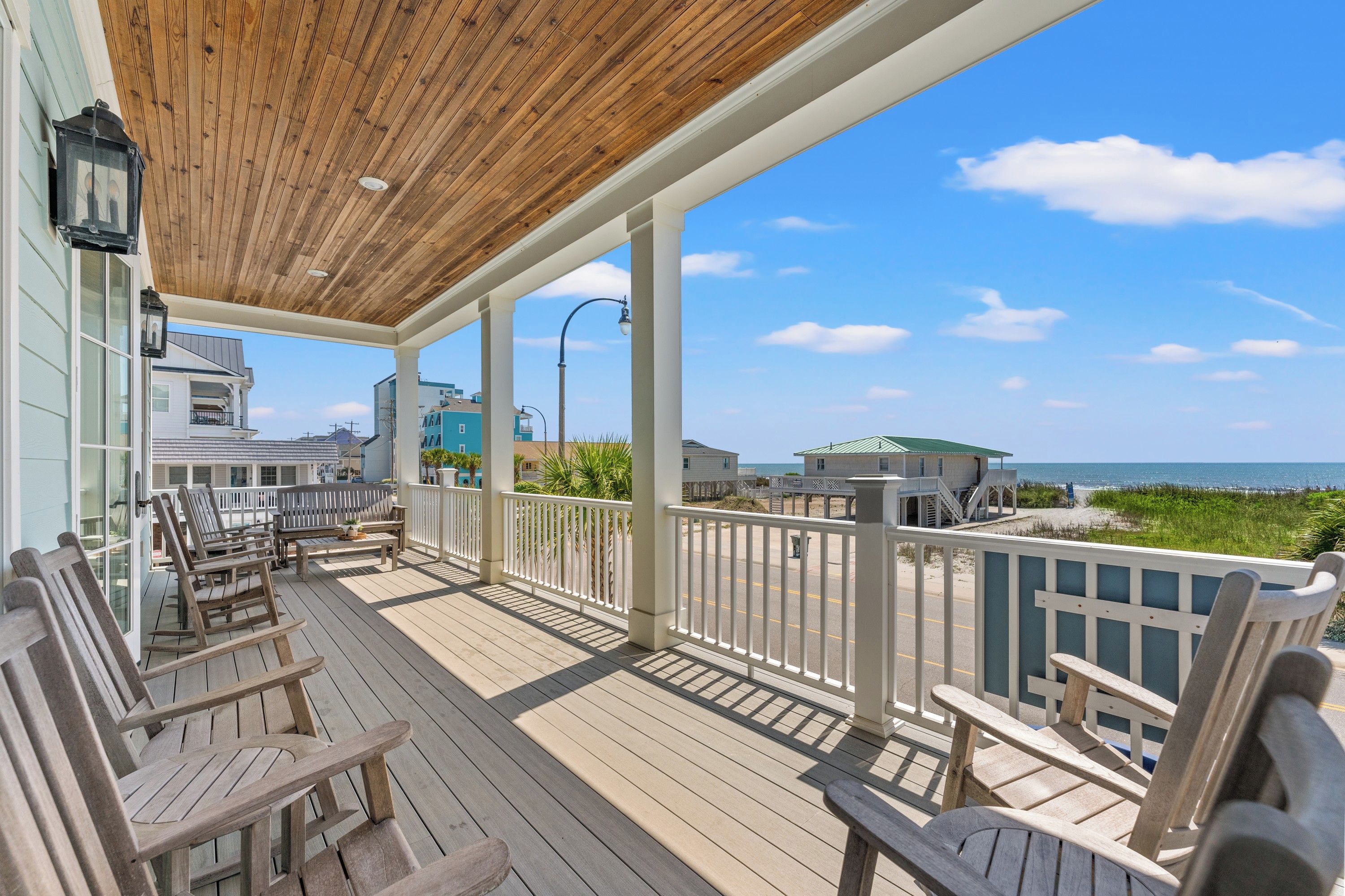 A wooden deck with outdoor seating, overlooking a beach and ocean.