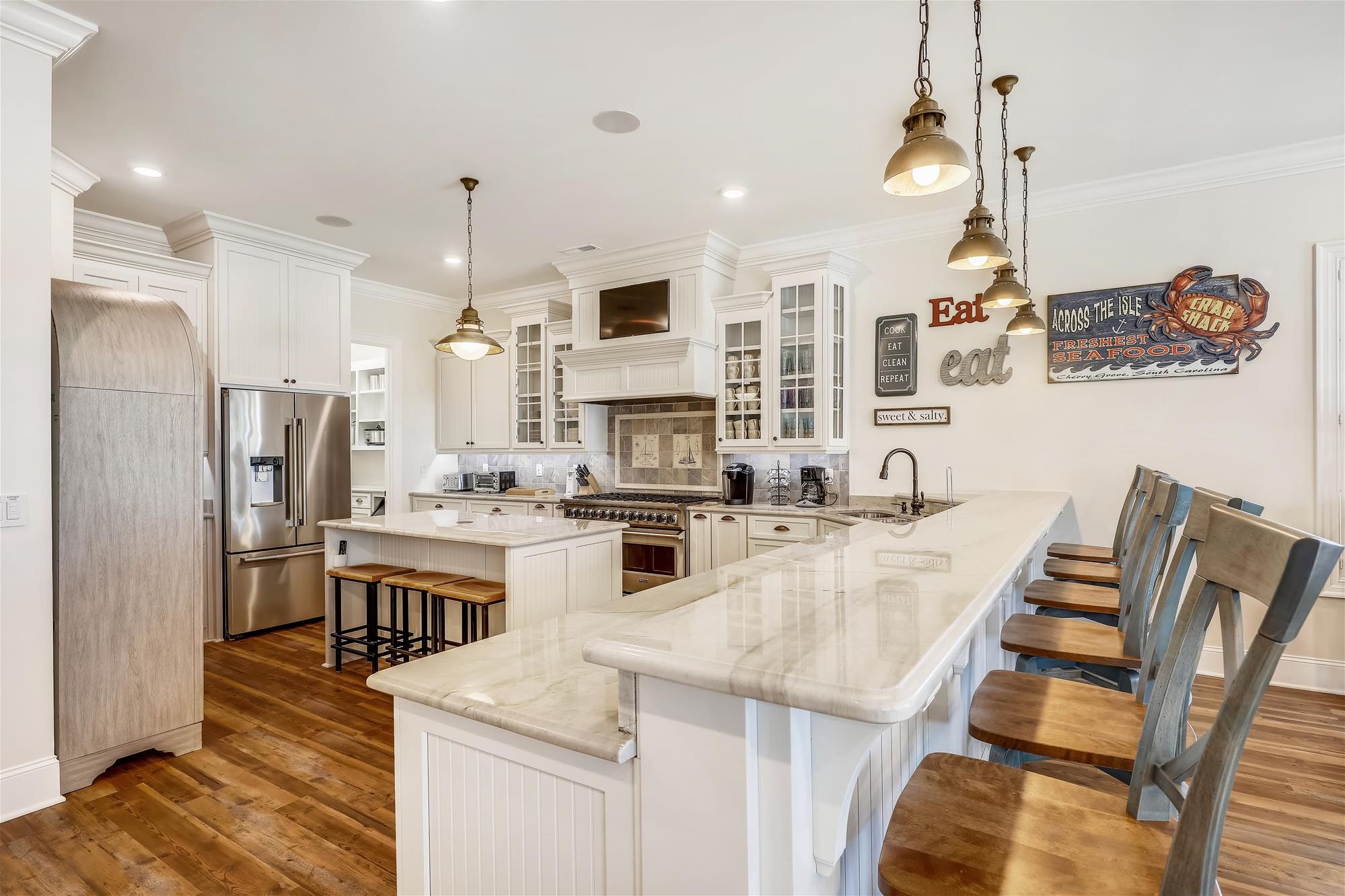 A spacious kitchen with white cabinetry, a large island, stainless steel appliances, and hanging pendant lights.