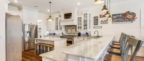 A spacious kitchen with white cabinetry, a large island, stainless steel appliances, and hanging pendant lights.