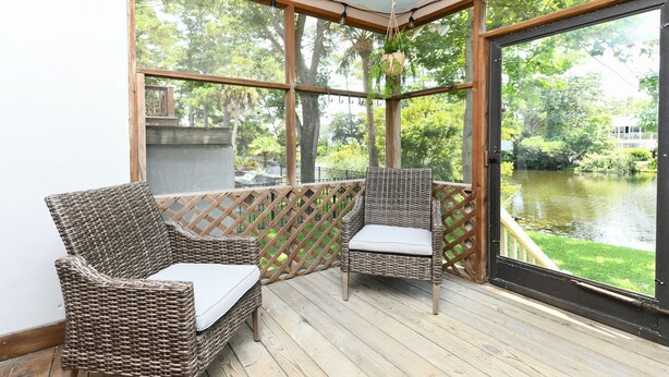 A covered outdoor seating area with wicker furniture and a view of a pond.