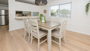 A dining area with a wooden table and four chairs, a kitchen with a microwave and stainless steel appliances, and a window with blinds.