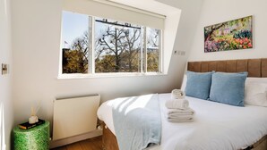A bedroom with a large window, a bed with white linens, blue pillows, and a painting on the wall. - Soho by Excel Apartments (London)