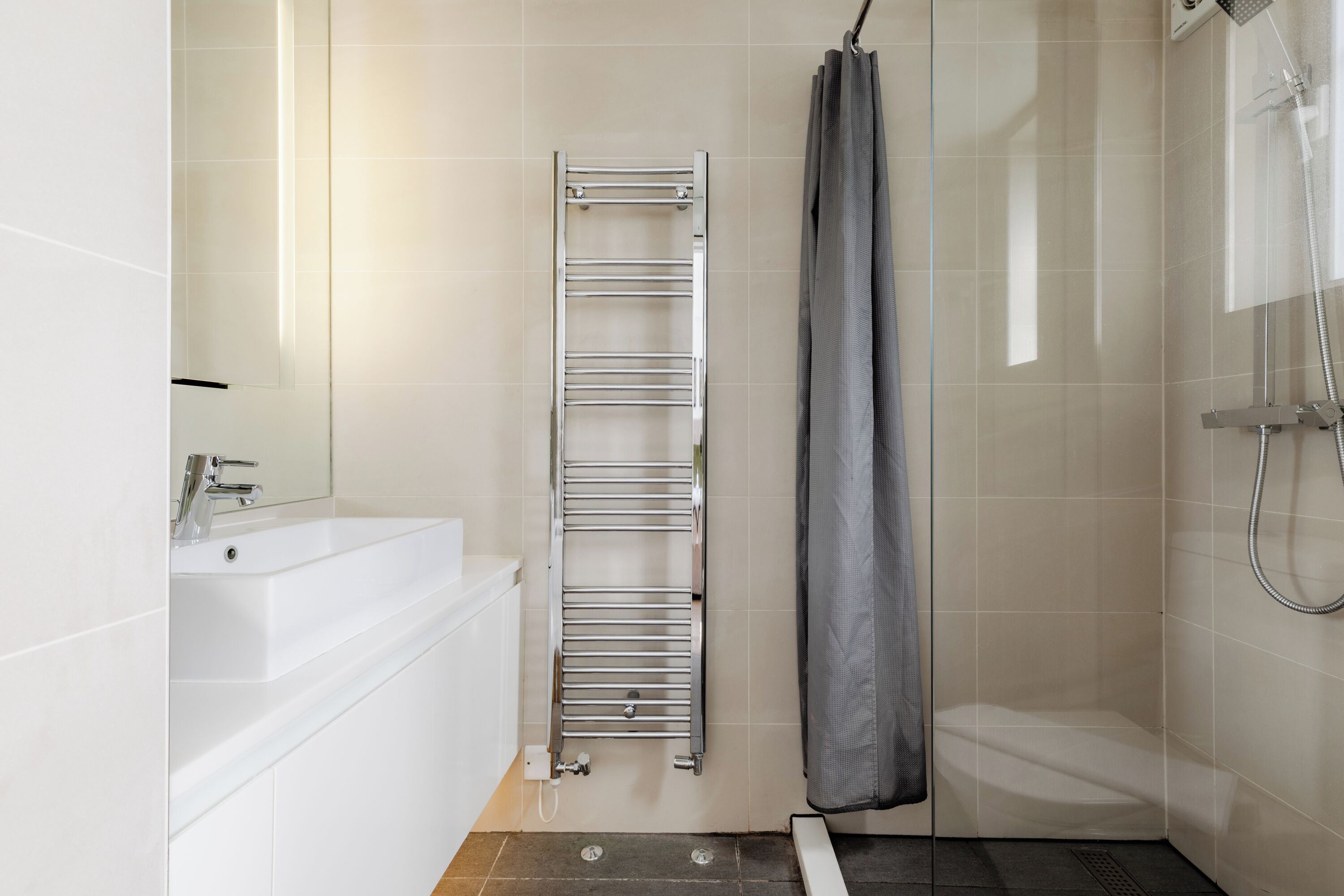 A modern bathroom with a white sink, a chrome towel rack, a shower with a glass door, and a shower curtain.