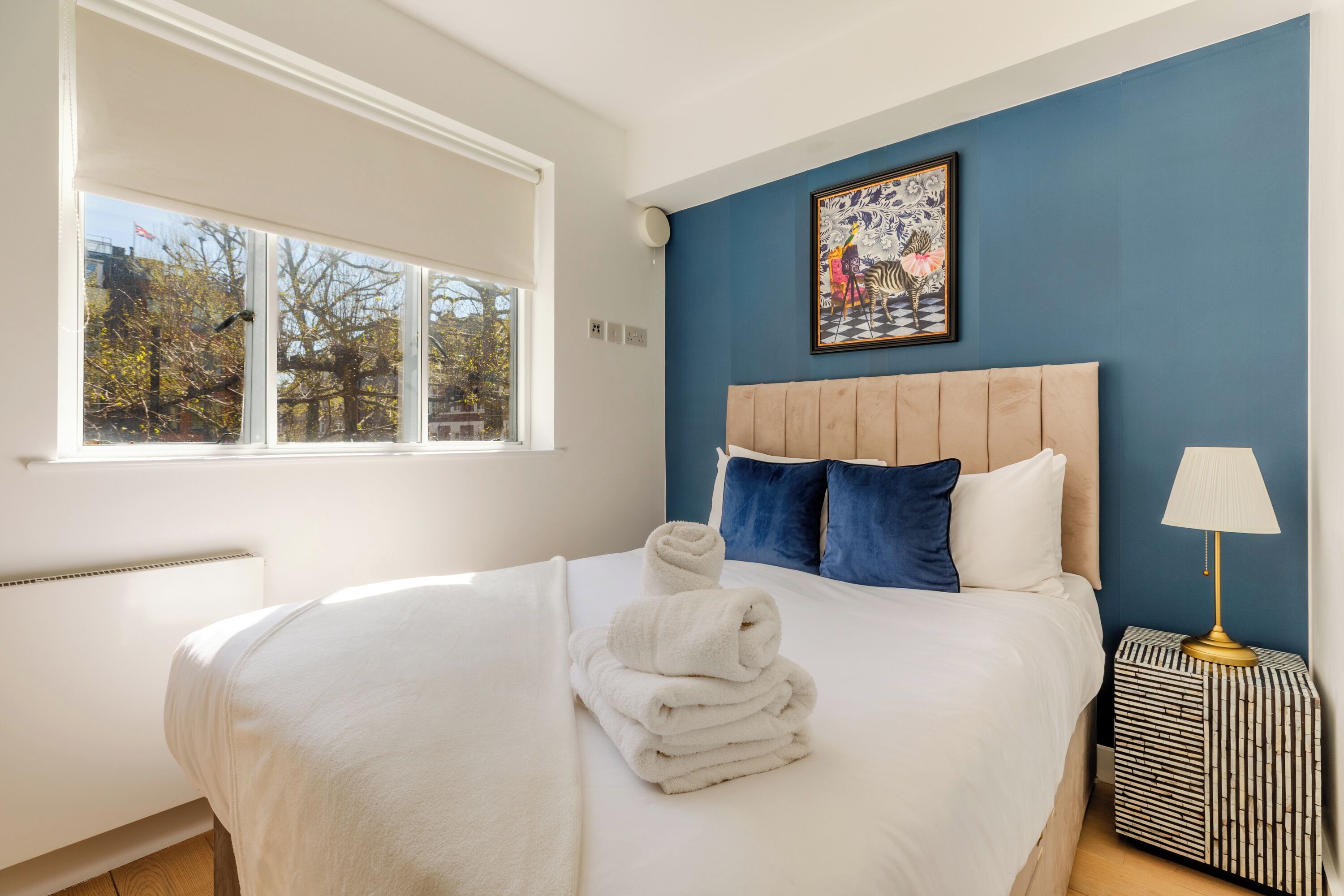 A neatly made bed with a folded towel, a headboard, and a wall-mounted painting.