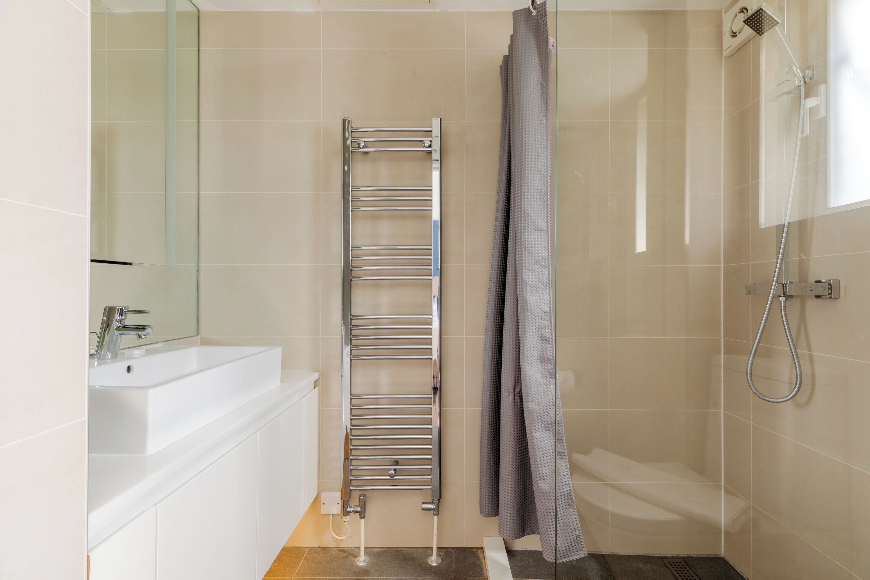 A modern bathroom with a white sink, a chrome towel rack, a shower with a handheld showerhead, and a glass shower enclosure.