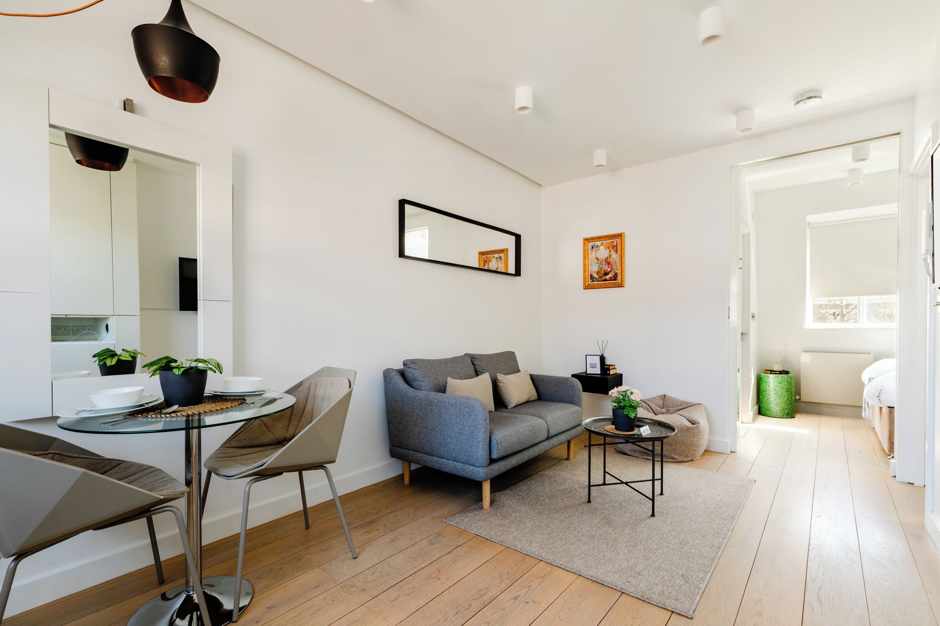 A modern living room with a glass dining table, grey sofa, and a small coffee table.