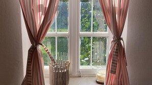 Uma janela com cortinas listradas amarradas e um banquinho junto à janela, com uma vela no parapeito.